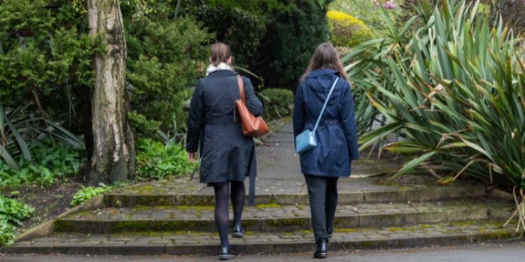 Photograph taken from behind of two women walking through a park.