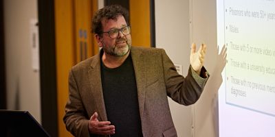 Man stands in front of projector screen whilst giving talk