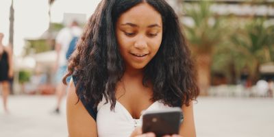 Pre-teenage girl uses mobile phone while sitting on the waterfront.