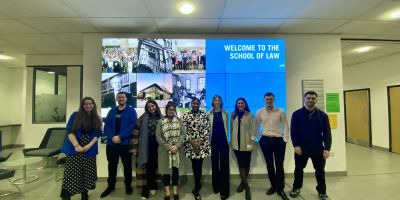 A group of alumni stand in front of the digital screens in the liberty building, side by side and smiling.