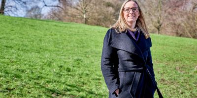 Portrait of Anna smiling and standing in a park.  Daylight and bright sunshine.