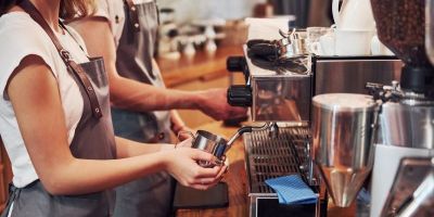 Close up of two baristas working behind the counter making coffee. Only their hands, arms and aprons are visible.