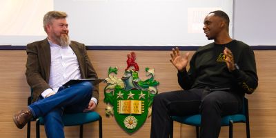 Dr Nick Cartwright and Dwayne Hutchinson speak to each other while sitting on chairs next to each other.