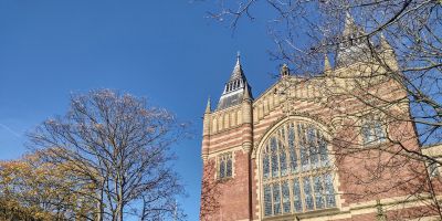 Picture of the Great Hall at the University of Leeds, a red brick building, surrounded by trees.