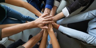 A group of diverse people standing in a circle with their hands stacked together in the centre.
