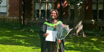 Alumna Pearls Eddo wearing her graduation gown, she's smiling.