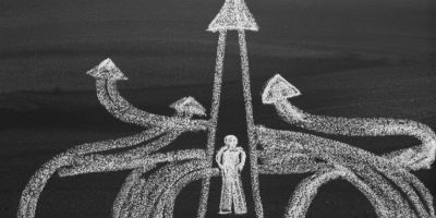 A chalk drawing on a blackboard shows a person standing at a crossroads with several arrows pointing in different directions.