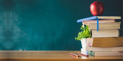 Stack of books in front of a blackboard with an apple on top.