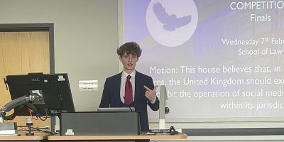 Alex standing in front of a big screen at the front of a lecture theatre wearing a suit
