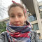 White woman, hair tied back, smiling into camera, wearing black leather jacket with a blue, white, and red chunky scarf on.