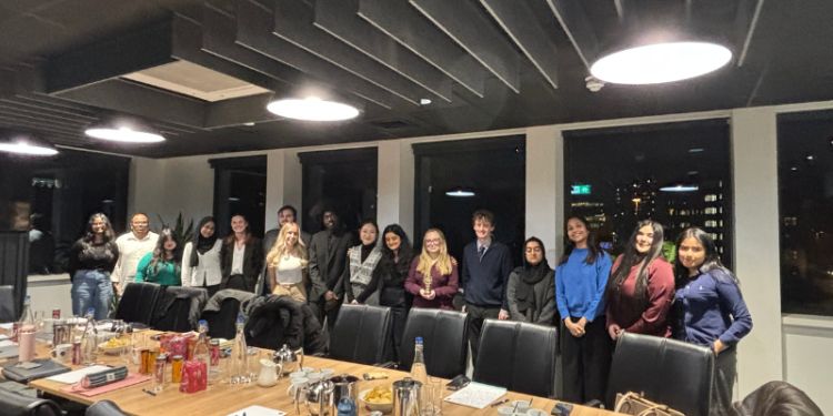 Group of students standing behind a boardroom table facing the camera