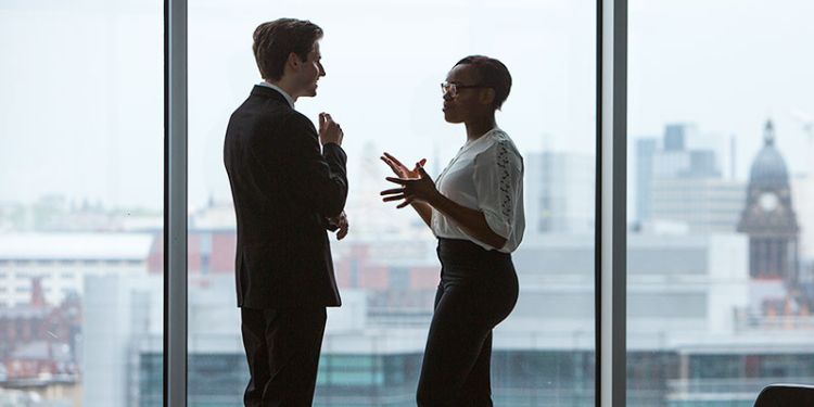 Two postgraduate students talking in front of a window with Leeds city in the background