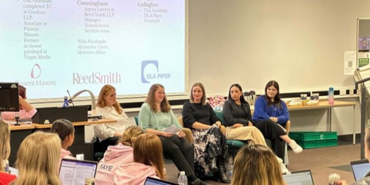 Five women sitting in a row at the front of a lecture theatre.