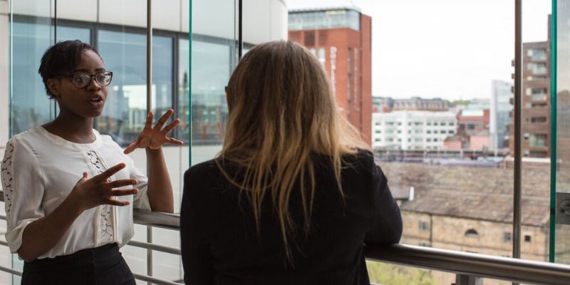 Two members of the University talk to each other next to a window