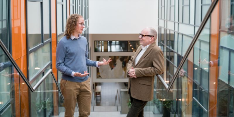 Photo of two men talking at the top of a set of stairs.